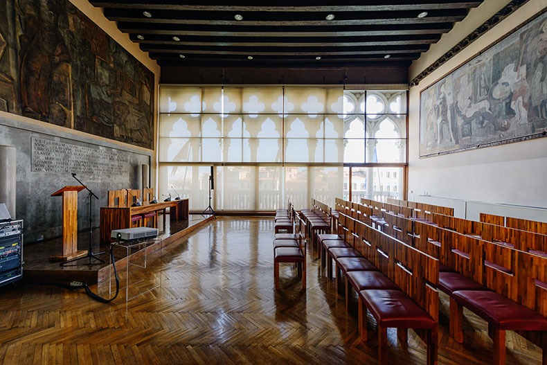 a grand lecture hall in Venice with large windows looking out on to a canal
