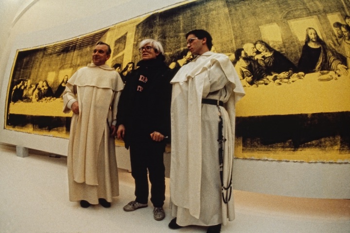 Andy Warhol in front of The Last Supper (Yellow) (1986) at the opening of Andy Warhol – Il Cenacolo at Palazzo delle Stelline, Milan, January 22, 1987. © Archivio Garghetti. Courtesy Gagosian.