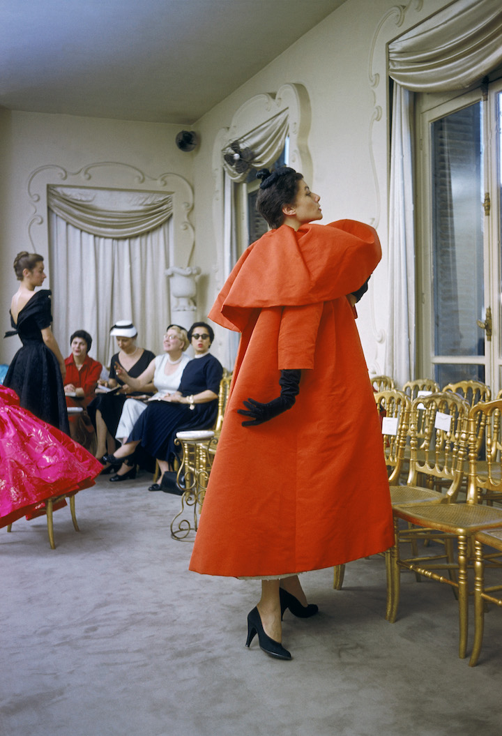 Model wearing Balenciaga orange coat as I. Magnin buyers inspect a dinner outfit in the background in Paris, 1954. © Mark Shaw / mptvimages.com