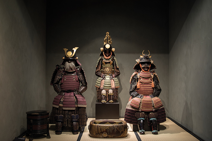 An open display platform in the museum, with a tachido tosei gusoku armour signed by Joshu Ju Saoteme letada and dated 1702 to the right of a boy's armour from the 18th century (centre).