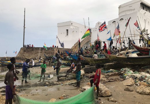 Fishermen in front of Cape Coast Castle, Ghana, with a staircase on the left leading up to a ‘Door of No Return’.