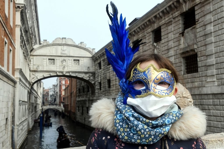 A tourist in Venice on 24 February 2020, wearing a protective face-mask and a Carnival mask.