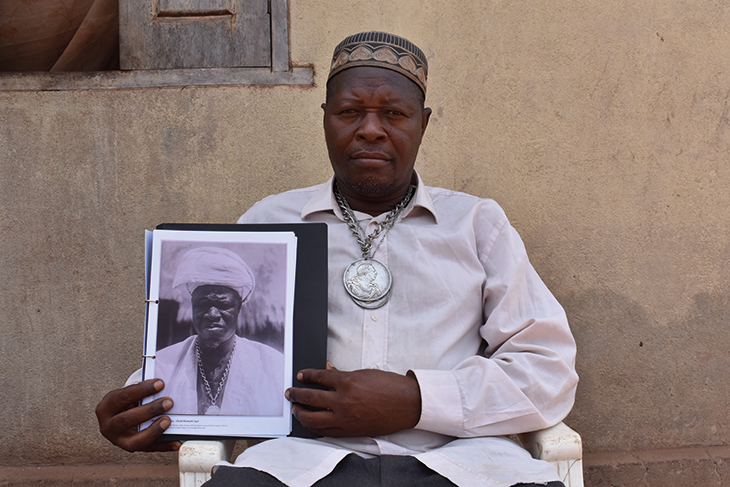 Paramount Chief Kandeh Sori Kakanday III of Samaya, Sierra Leone, holding a photograph of his ancestor, Chief Almamy Suri Kandeh, taken by Northcote Thomas in 1914.