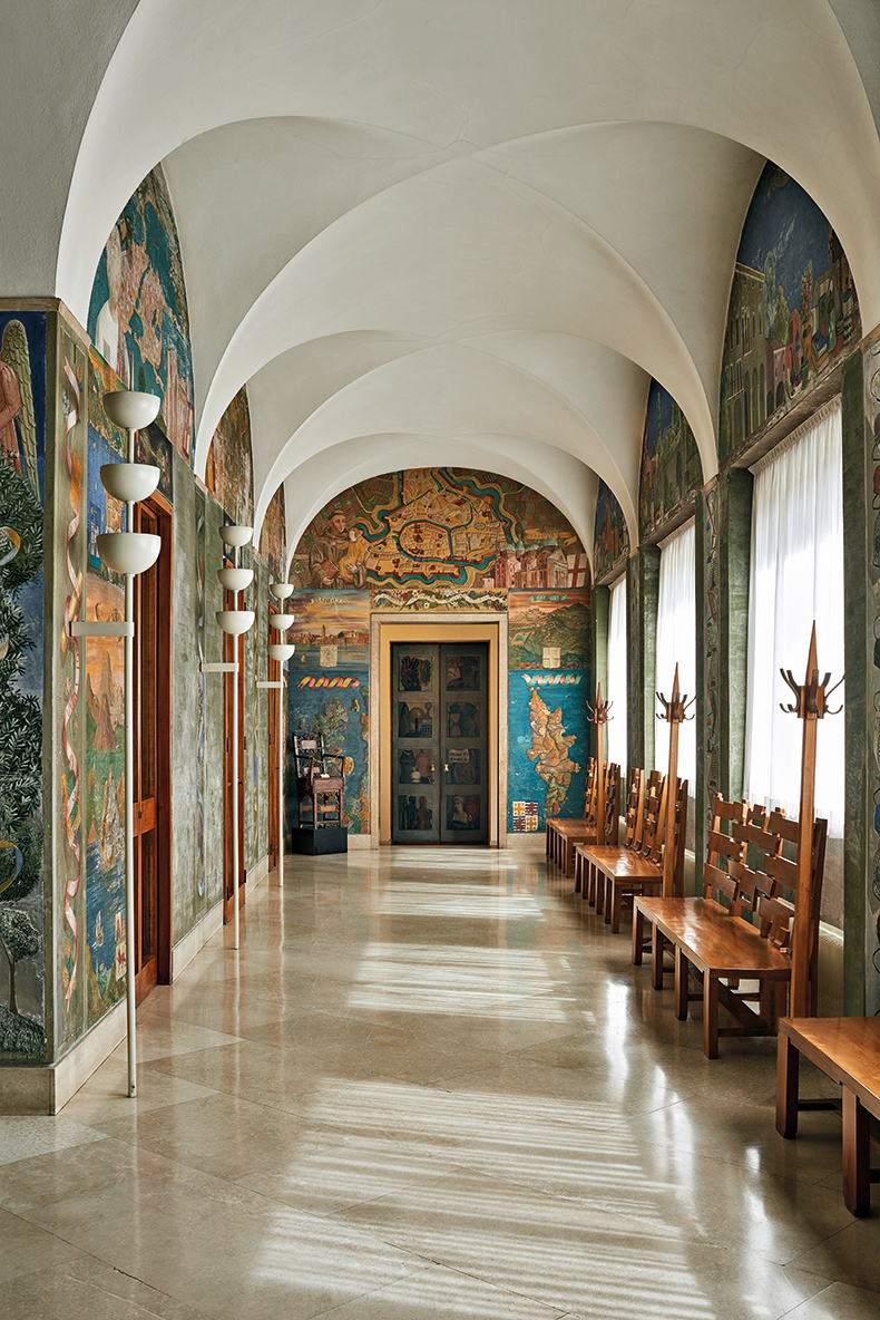 Murals by Fulvio Pendini and Piero Fornasetti form a backdrop to furniture by Gio Ponti in the Galleria del Rettorato in Palazzo Bo.