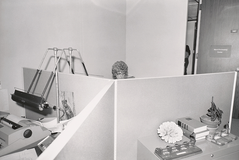Head of female worker seen over office cubical, Standard Oil Company of California (1976–77), Chauncey Hare. From Quitting Your Day Job: Chauncey Hare’s Photographic Work by Robert Slifkin (MACK 2022). Chauncey Hare Photograph Archive.