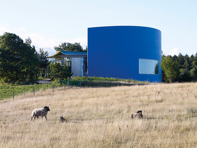 A blue building with rounded walls in a sheep field